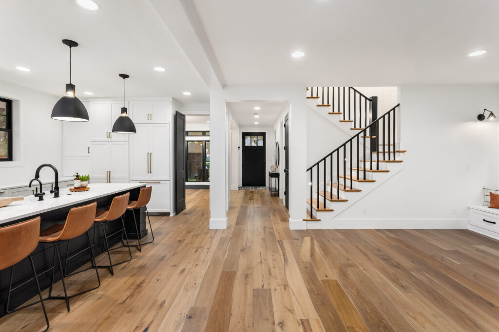 the interior of a custom home built by C4 Builders. a kitchen island and chairs are on the left side and stairs on the right side, with real hardwood floors